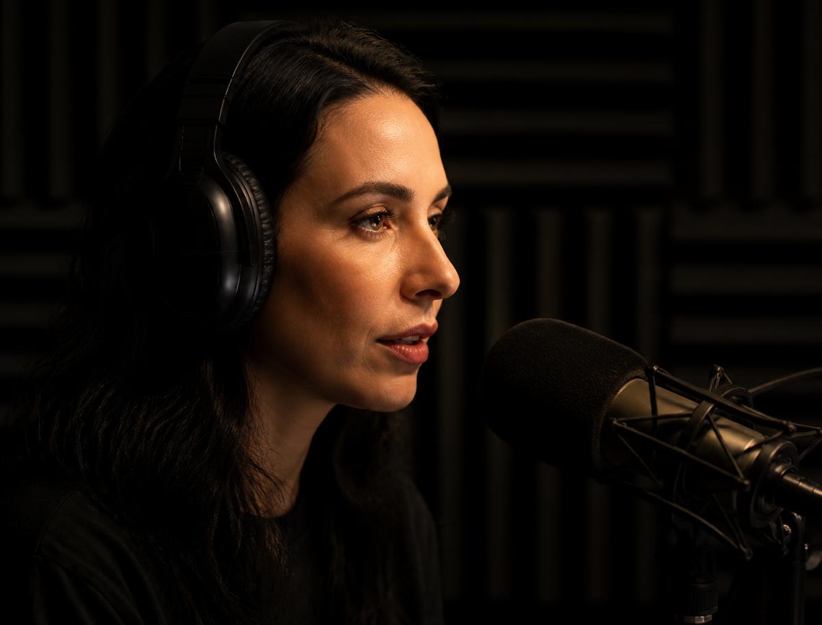 Woman speaking into a studio microphone in a dark booth